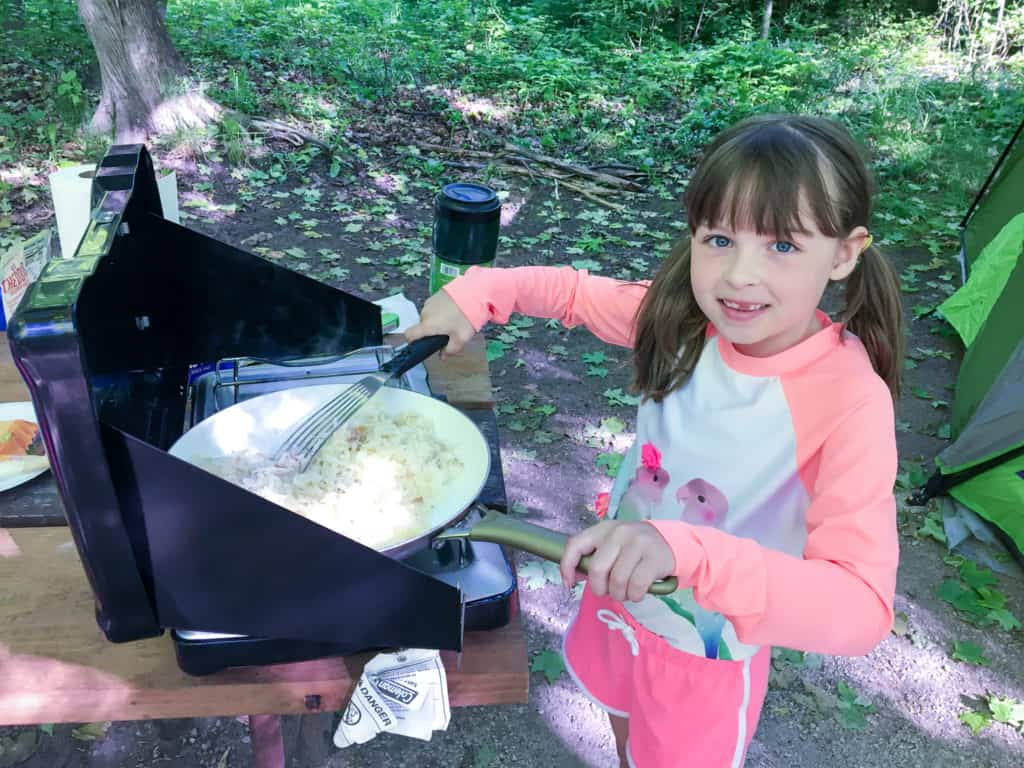 Young girl cooking potatoes over a camp stove in a wooded area