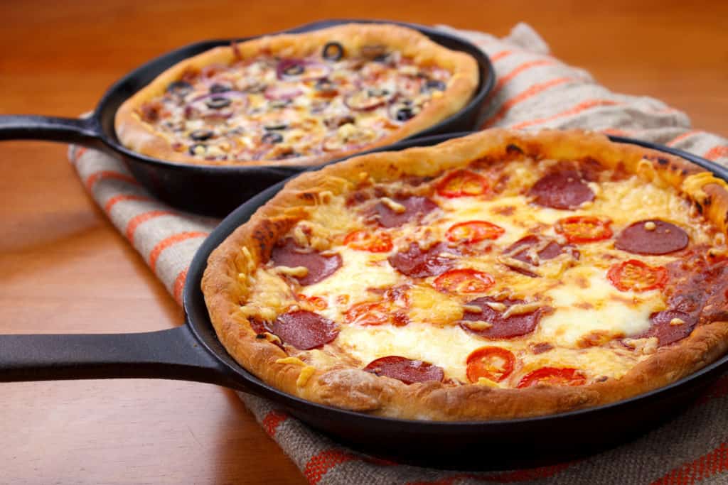 Two cast iron skillet pan pizzas on wooden table