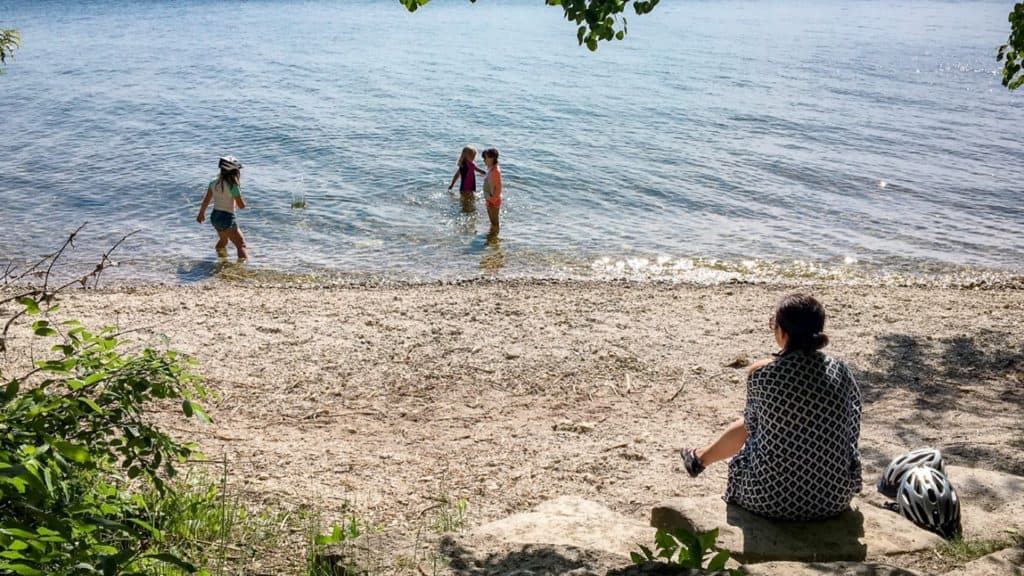 Three young girls wading in a large lake while their mom watches